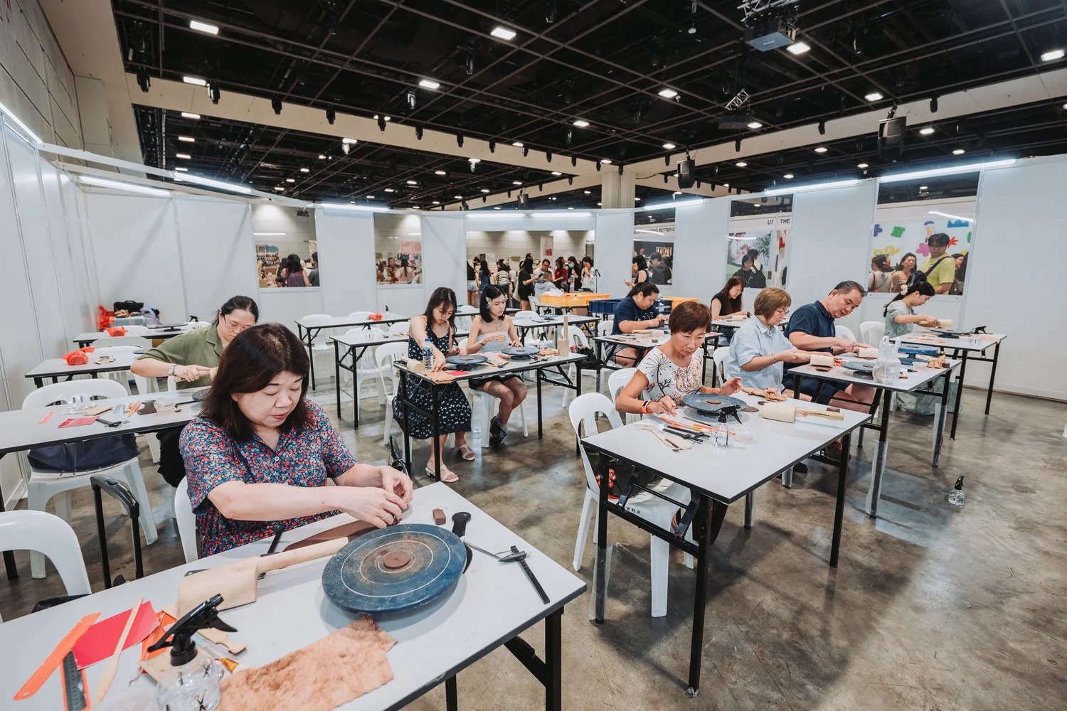 Visitors at white tables working on leathercraft and clay in a hands-on workshop zone at Asia Art & Craft Fair 2026 in Singapore