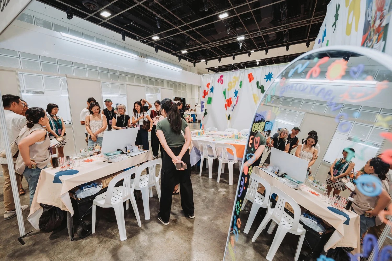 A group gathers around workshop tables beside a painted mirror installation at Asia Art & Craft Fair 2026 in Singapore