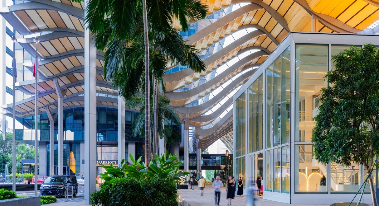 Ground-level walkway at South Beach, Singapore, under the wave-shaped canopy, with palms and a glass pavilion