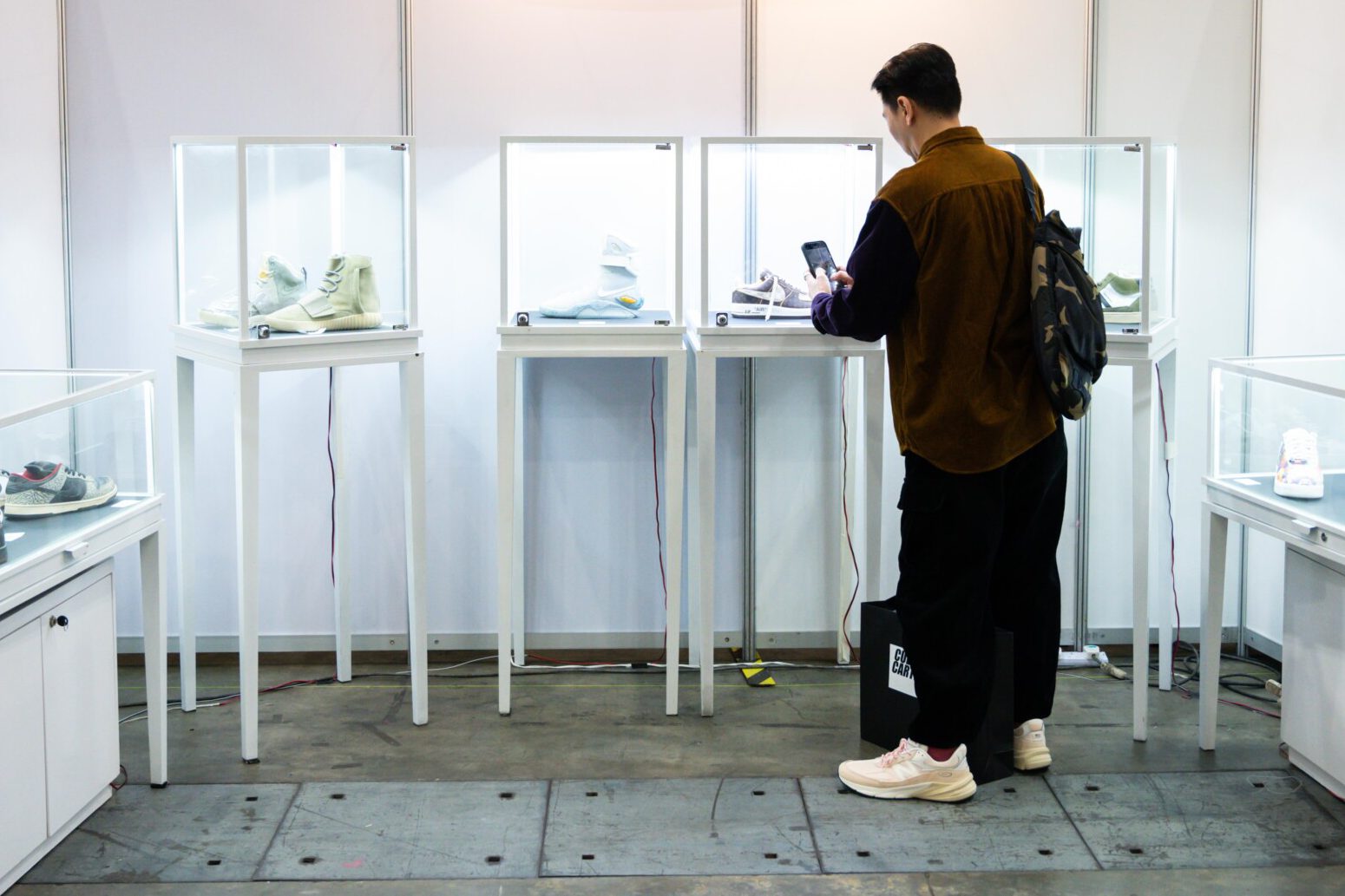 A visitor photographs rare sneakers in lit glass cases at Culture Cartel 2025, Singapore Expo