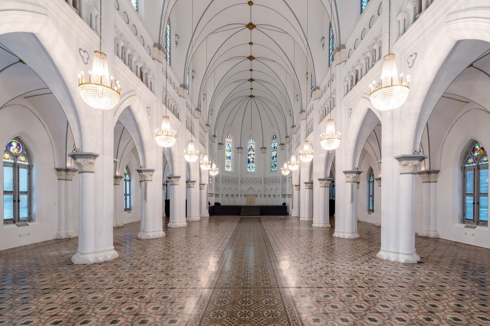 Empty interior of CHIJMES Hall in Singapore, a former Gothic chapel with white columns, crystal chandeliers, stained glass and patterned floor tiles
