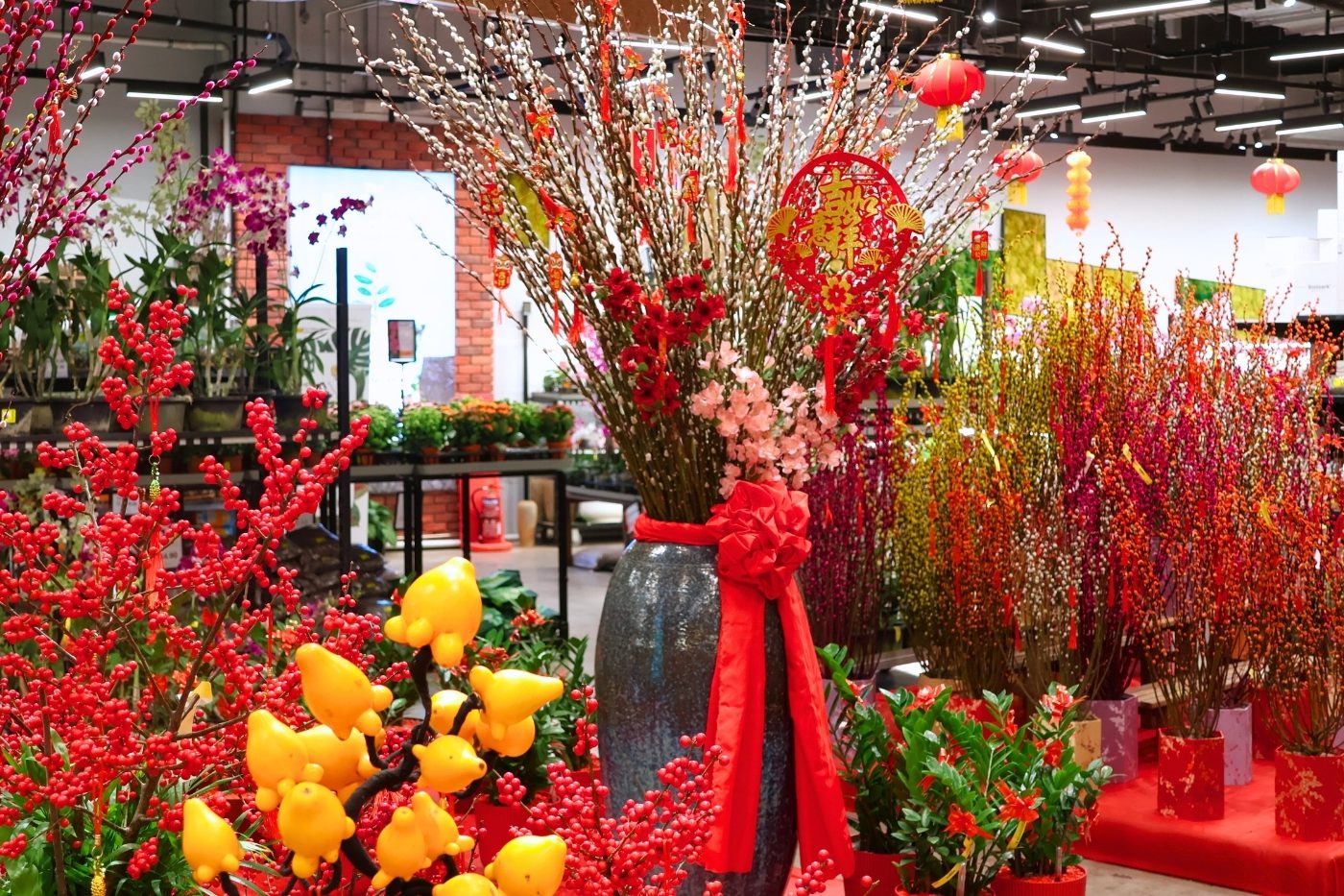 A tall vase of pussy willow hung with red Chinese New Year ornaments among festive plants on the shop floor at Far East Flora Centre, Singapore