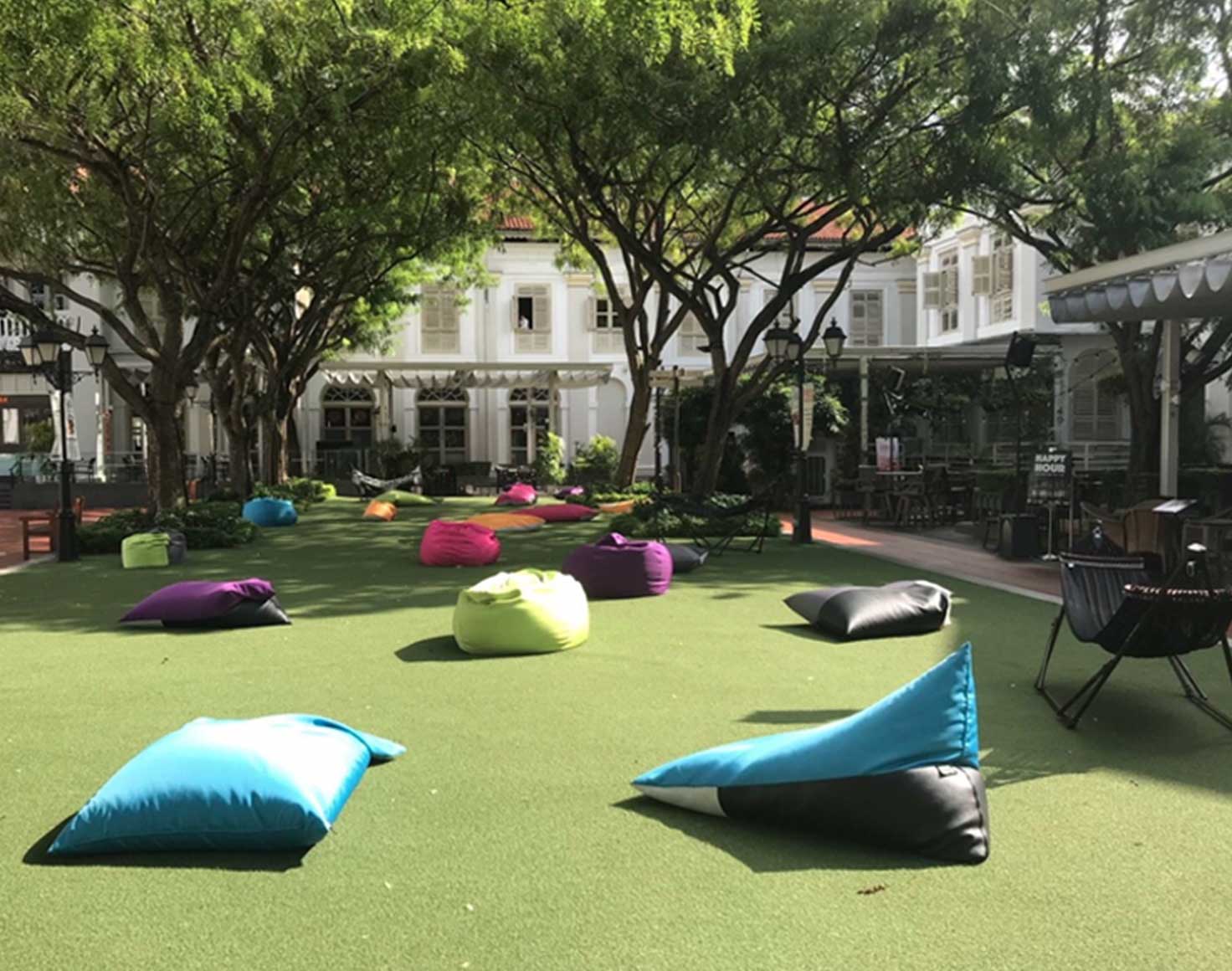 The lawn in the CHIJMES courtyard on a sunny day, scattered with bean bags under rain trees and ringed by white colonial buildings, Singapore