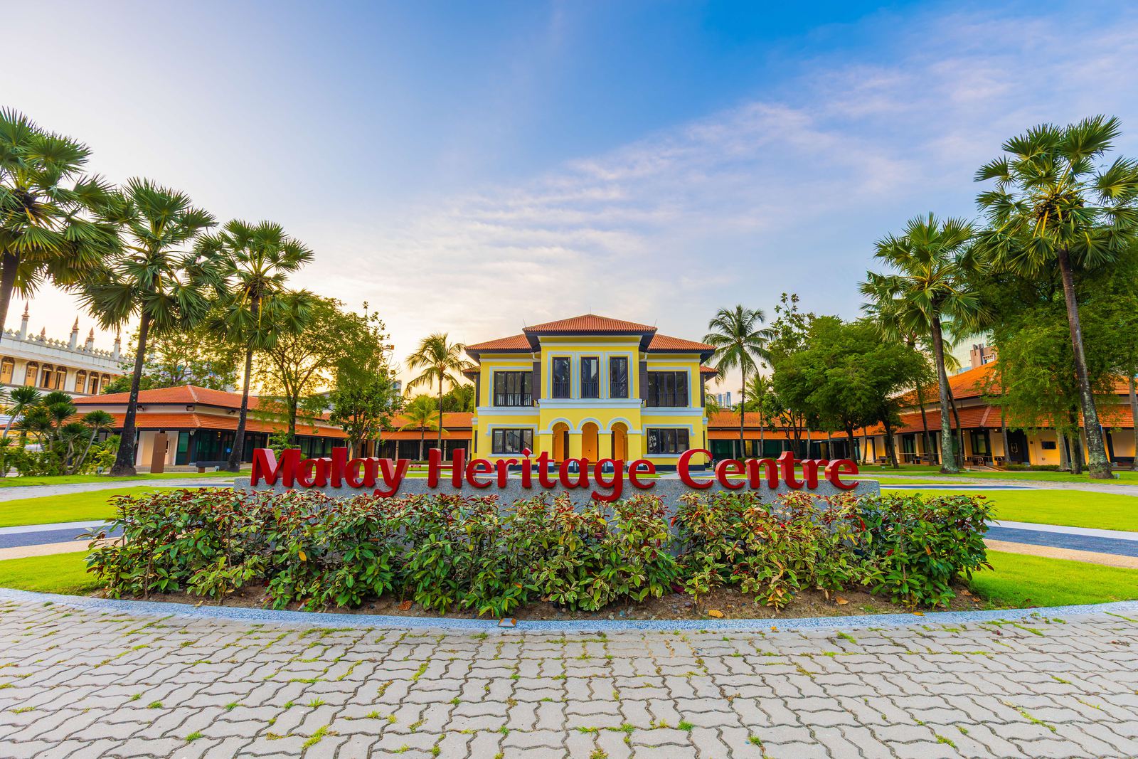 Red 'Malay Heritage Centre' lettering in a flower bed in front of the centre's yellow building and lawn, Kampong Gelam, Singapore