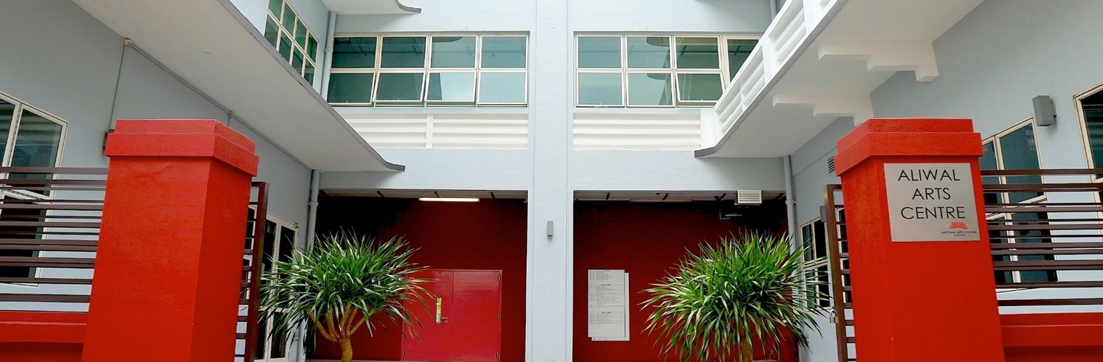 Courtyard entrance of Aliwal Arts Centre in Singapore, with red gate pillars, potted palms and a red inner wall