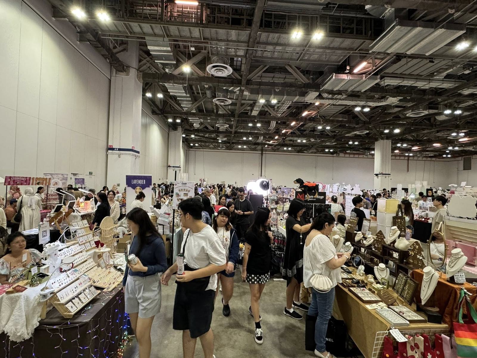 Shoppers walk a busy aisle of jewellery and craft stalls strung with fairy lights inside a Marina Bay Sands Expo hall in Singapore
