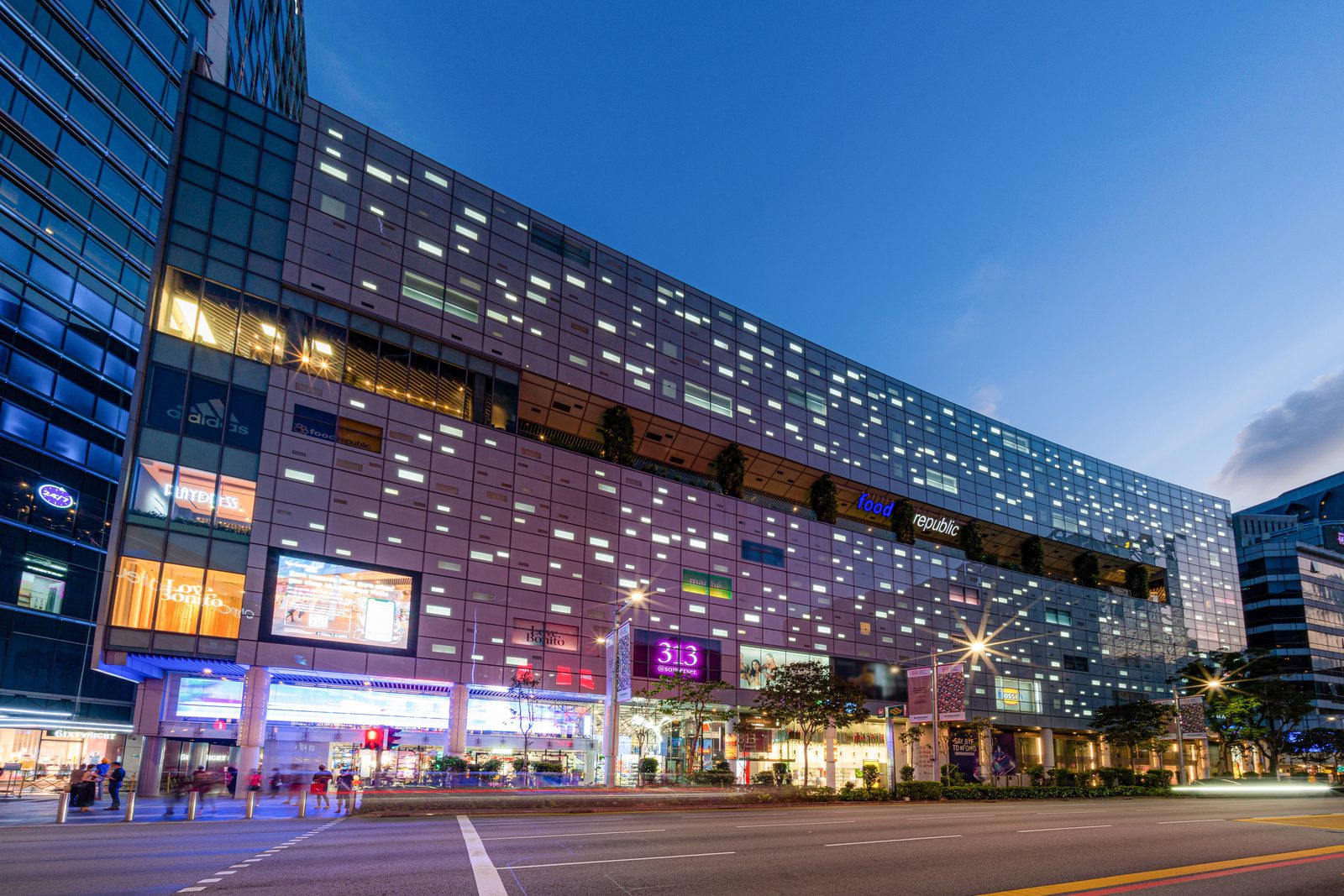 The Orchard Road frontage of the 313@somerset shopping mall in Singapore at dusk, with its lit facade and street-level entrance