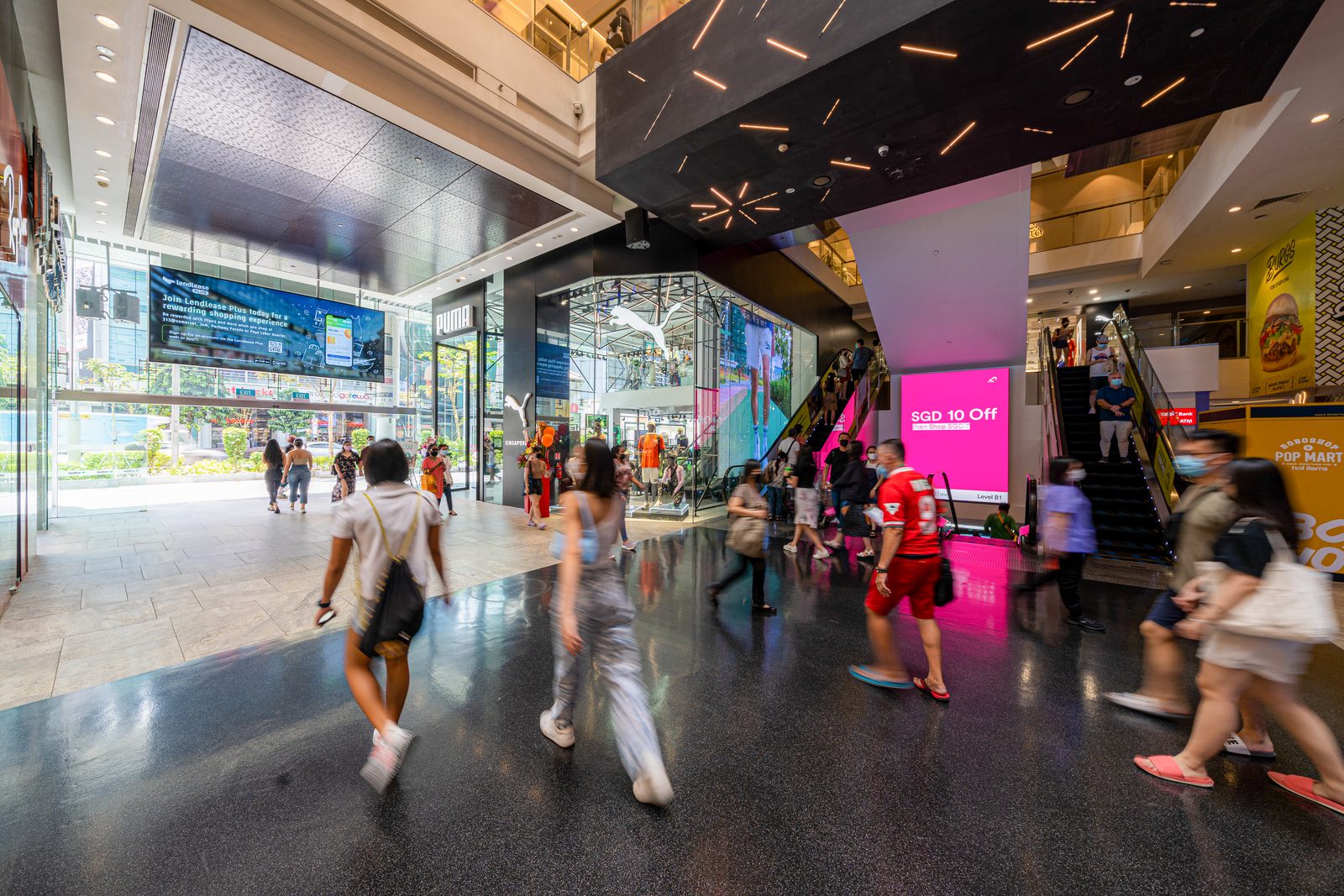 Shoppers walking through the Level 1 entrance concourse of 313@somerset in Singapore, beside the escalators and the Orchard Road doors